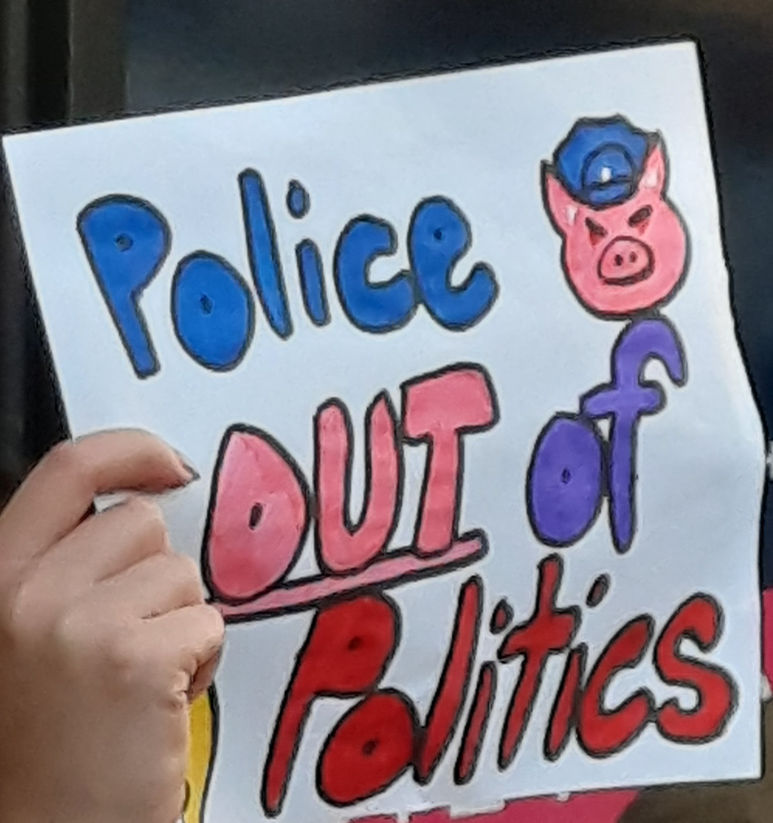 Poster being held saying Police Out of Politics. Image of a pig with a police hat.