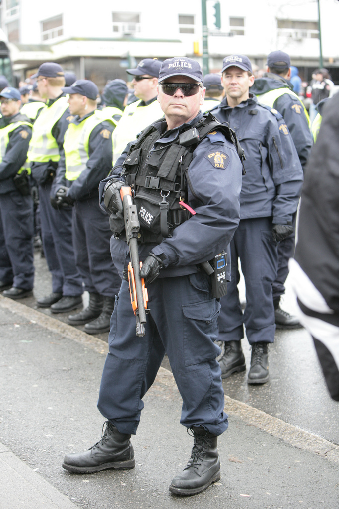 RCMP in riot gear. One standing with shotgun.