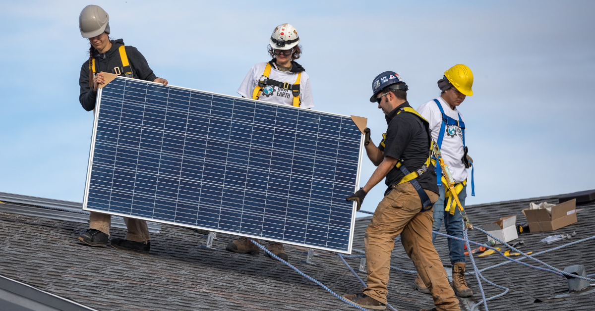 Members of Iron and Earth installign a solar panel on a roof.