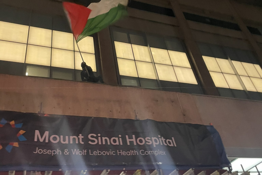 SPIDERMAN4PALESTINE WAVES A PALESTINIAN FLAG ABOVE THE ENTRANCE OF MOUNT SINAI HOSPITAL, ONE OF AT LEAST EIGHT ELEVATED SPOTS THEY CLIMBED TO IN THE COURSE OF THE RALLY ON FEB. 12. PHOTO CREDIT: ANNA LIPPMAN.
