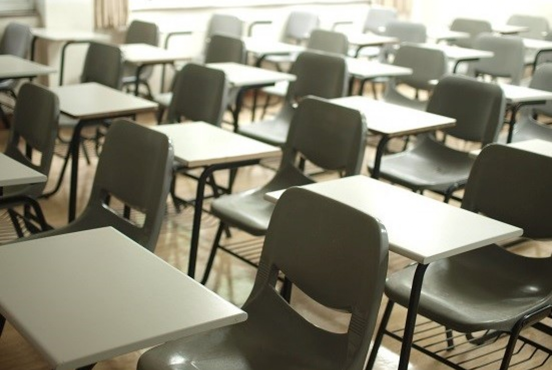 Photo of empty single grey desks in a classroom. Photo by MChe Lee on Unsplash