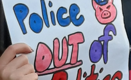 Poster being held saying Police Out of Politics. Image of a pig with a police hat.